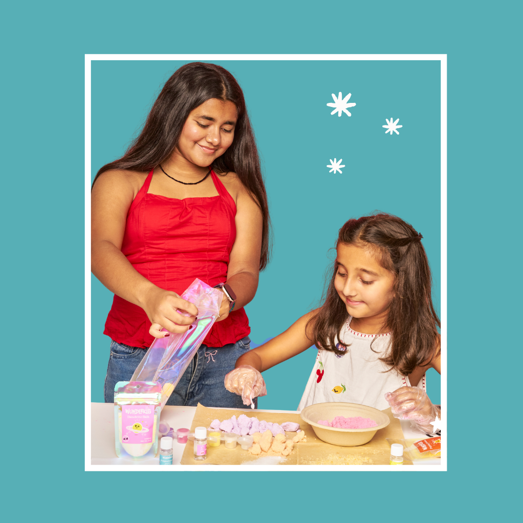 Two girls making bath fizz kit against a blue background with stars