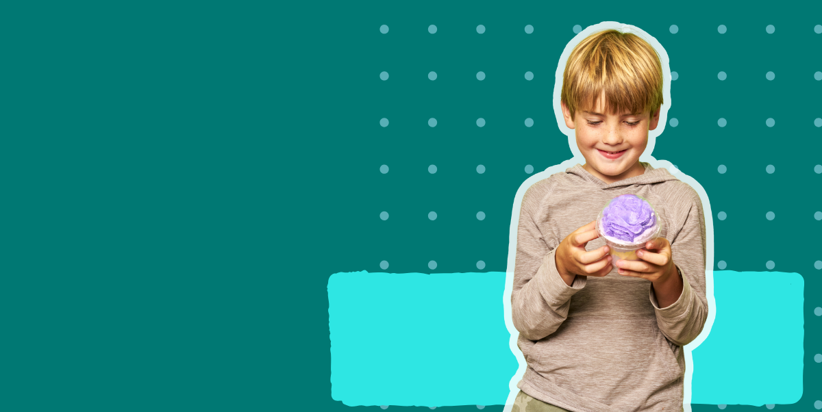 Boy holding DIY kit Rainbow Whirl milk bath cup against a green and blue background