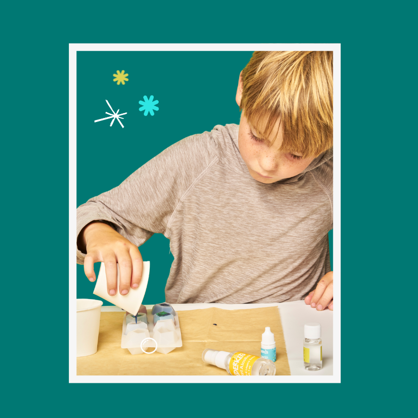 Child pouring soap into a mold on a table against a teal background